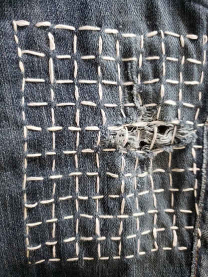First attempt. Hole and worn area in denim, stitched in a grid pattern in white embroidery thread. Sloppy looking.