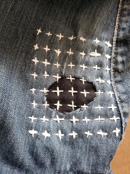 Second attempt. Same pair of jeans but different hole. For this one, I cut away all the worn out area and folded the edge under so the patching material is clearly visible. And I used a cross-hatch stitch in the same white thread. Much neater looking.
